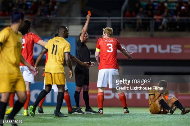 professional referee gives player red card as they argue after a rival player gets injured during international match - referee card stock pictures, royalty-free photos & images