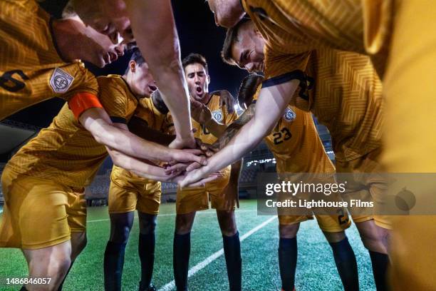 energetic team of male football players join their hands together in a team huddle before an international game - sportliga stock-fotos und bilder