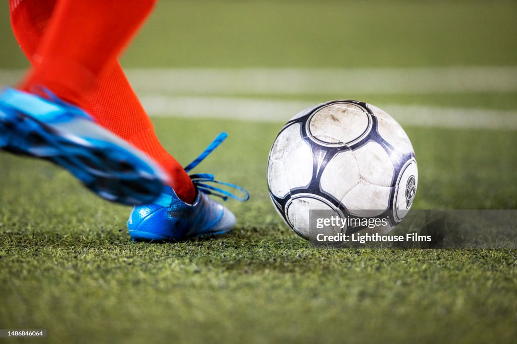 Athlete wearing cleats strikes a soccer ball on a grass field during a professional football match
