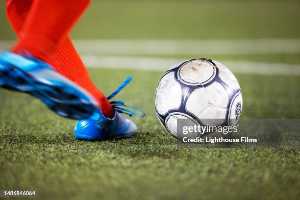 athlete wearing cleats strikes a soccer ball on a grass field during a professional football match - bola de futebol imagens e fotografias de stock