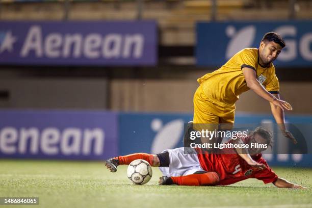 competitive professional football player does a slide tackle to steal the soccer ball and his opponent trips over him - foul sports stock pictures, royalty-free photos & images