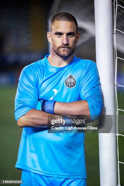 portrait of a professional soccer goalie as he leans against the net and looks at the camera - football player face stock pictures, royalty-free photos & images