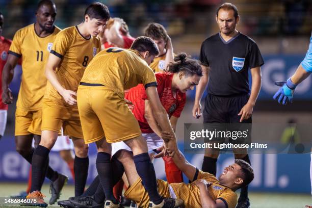 referee supervises as concerned soccer players check on an injured teammate and help him up during a professional game - professional sportsperson ストックフォトと画像