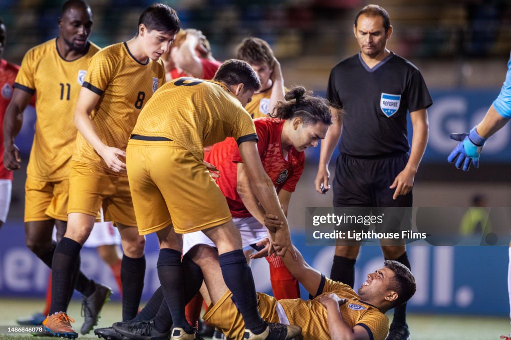 Referee supervises as concerned soccer players check on an injured teammate and help him up during a professional game