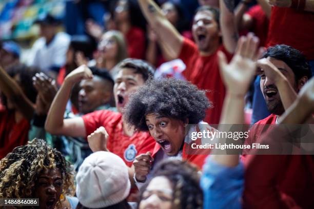 ecstatic sports fan makes shocked face and excitedly screams in crowd for favorite soccer team - internationaler fußball stock-fotos und bilder