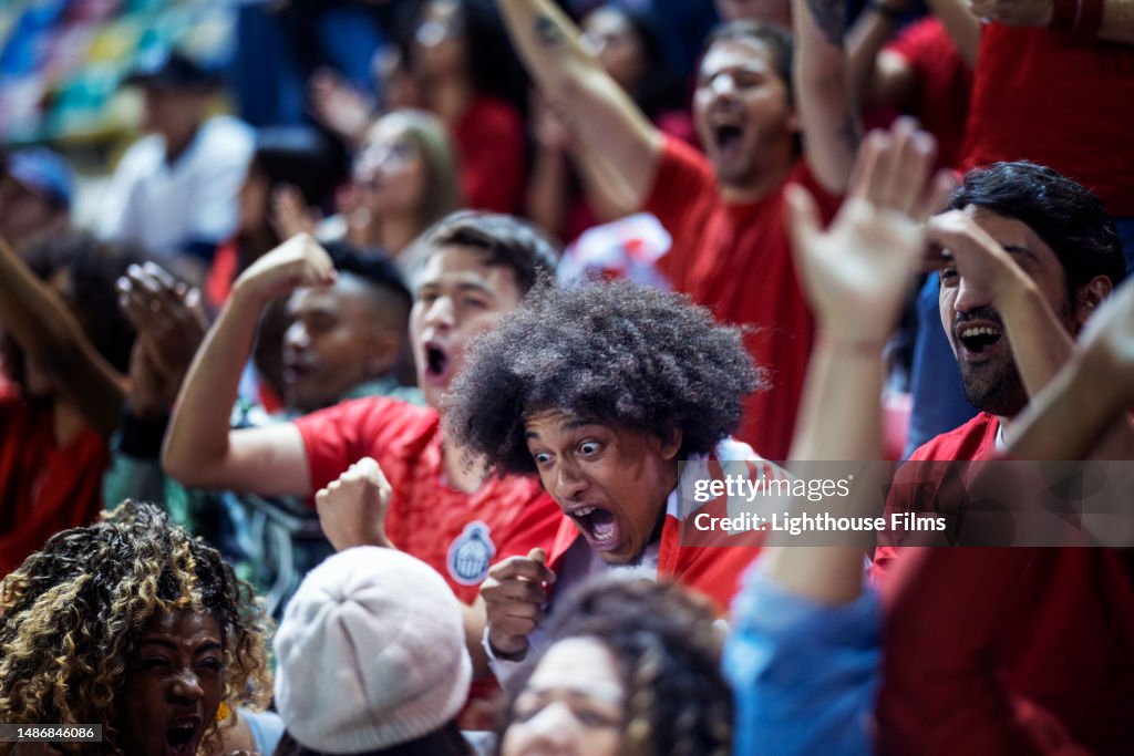 Ecstatic sports fan makes shocked face and excitedly screams in crowd for favorite soccer team