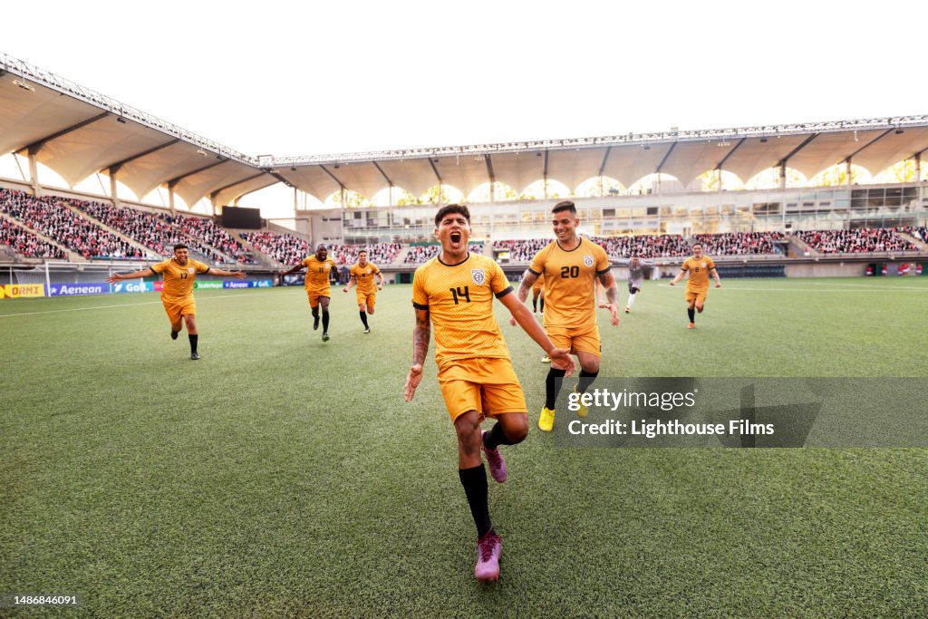 Ecstatic male soccer player runs down a stadium field cheering in celebration during an international match