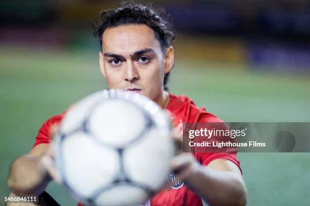 determined professional soccer player sits on stadium field and gives camera an intense look - mittelfeldspieler fußballspieler stock-fotos und bilder