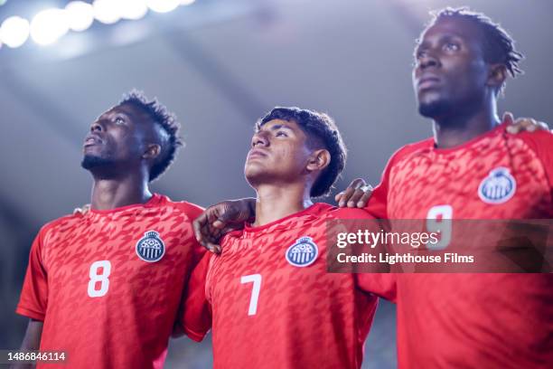 team of professional male soccer players stand on stadium field with arms around each other before big game - pre game huddle stock pictures, royalty-free photos & images