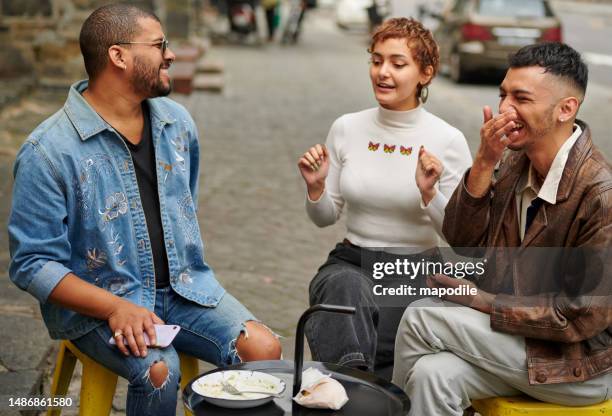 laughing friends talking over a snack outside on a city sidewalk - three people smiling stock pictures, royalty-free photos & images