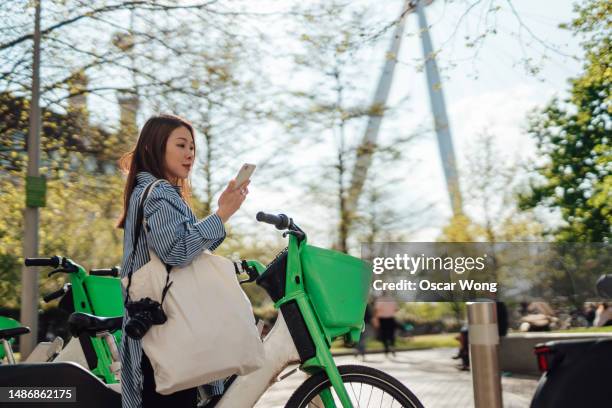 smiling asian female tourist using smartphone while exploring london with a bike - cycling stock pictures, royalty-free photos & images