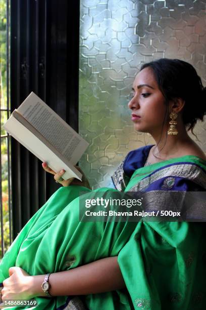 young woman reading book while sitting on window sill - judges robe stock pictures, royalty-free photos & images