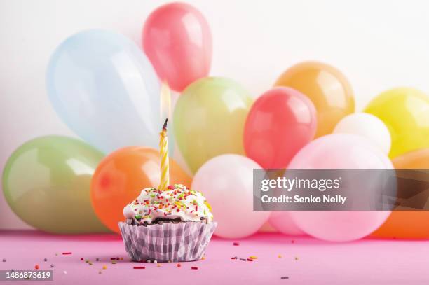 festive cupcake with one burning candle on background of balloons and copy space. - buttercream stock pictures, royalty-free photos & images
