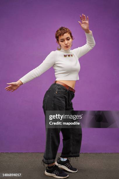 stylish young woman dancing against a purple wall outside - crop top stock pictures, royalty-free photos & images