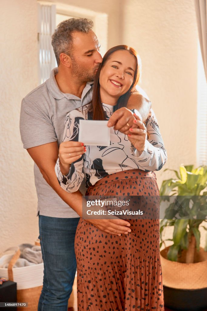 Photo, pregnancy announcement and portrait of a woman with a man and kiss holding a picture at home. Happiness, love and support of a pregnant female person with a sonogram in a house with husband