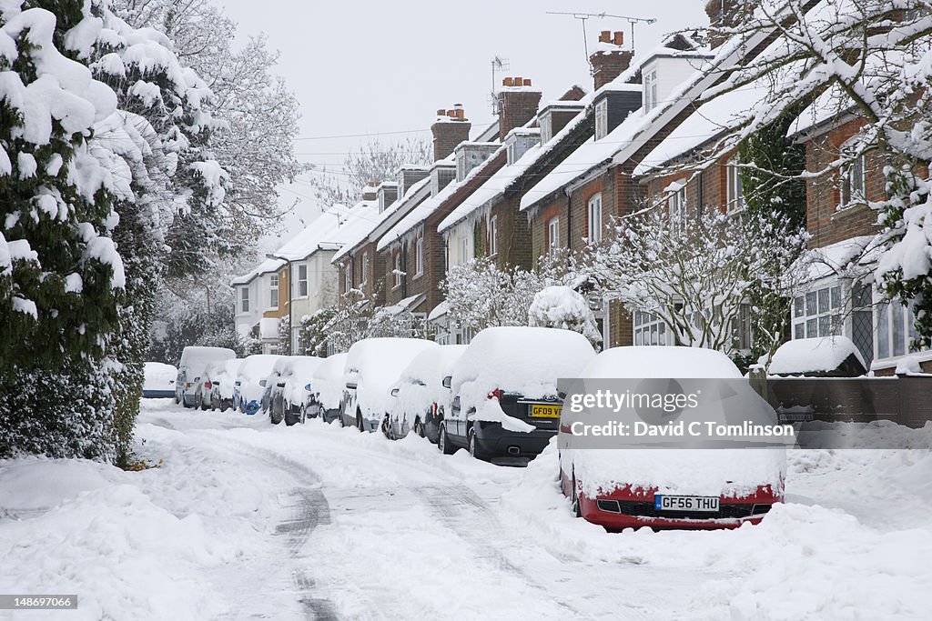 Parked cars in residential street covered in thick snow after blizzard.