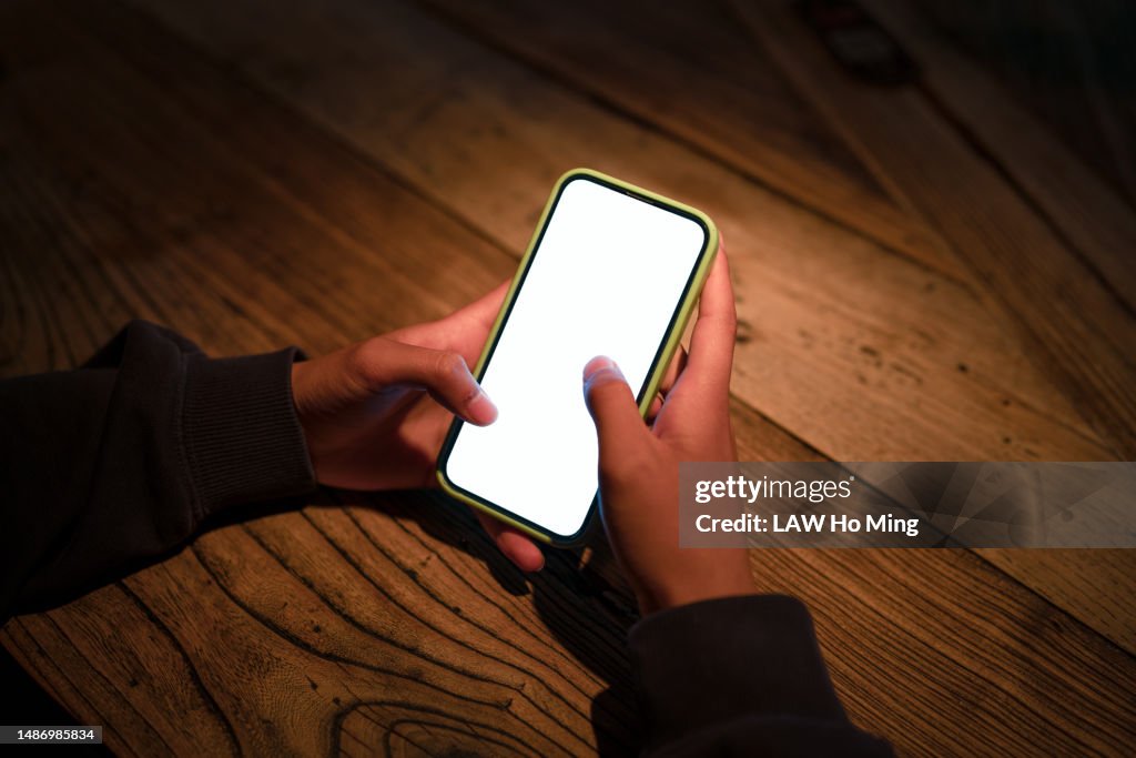 A pair of hands using the phone in the light.