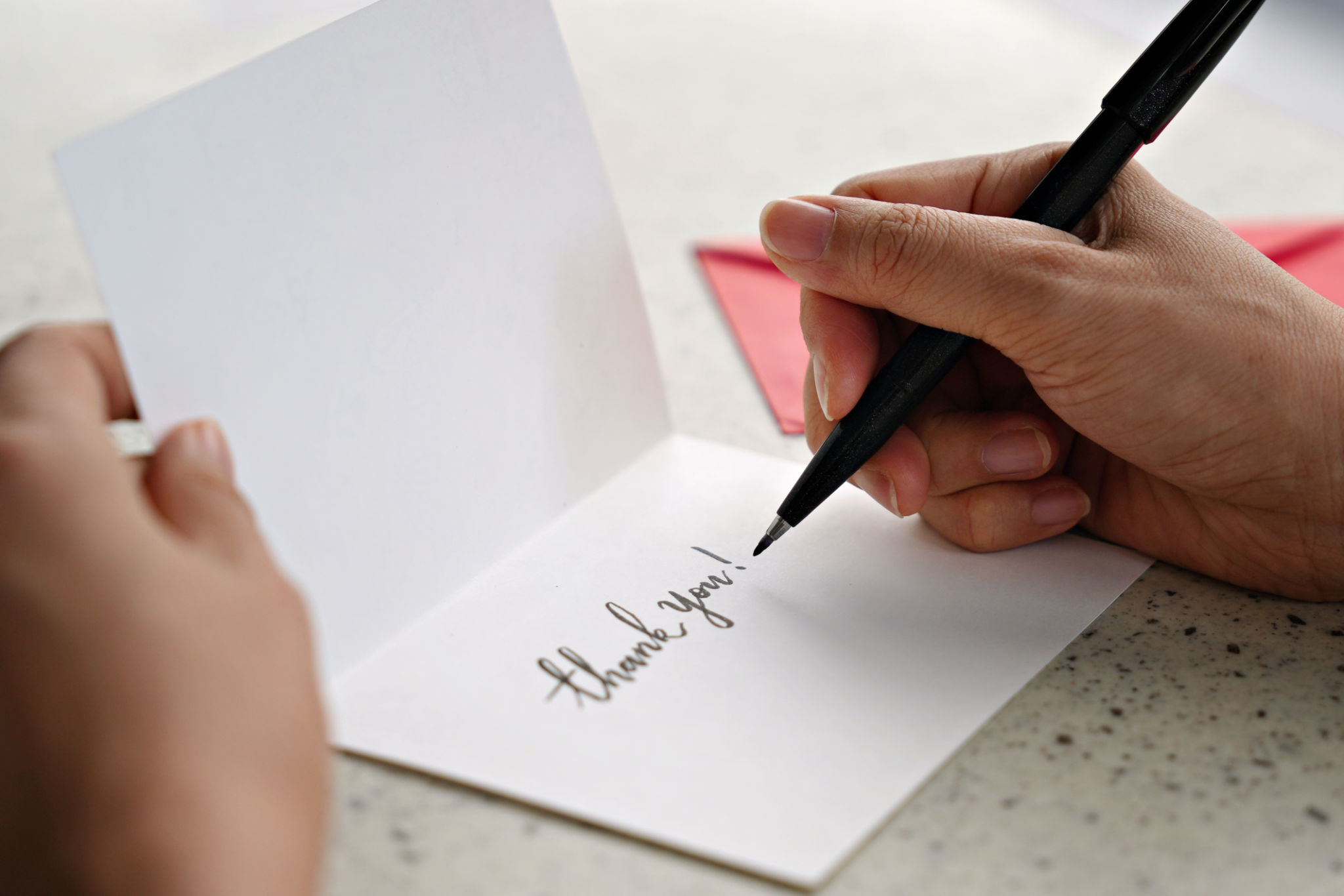 A woman hands writing a Thank You note on a greeting card with red envelope A woman hands writing a Thank You note on a greeting card with red envelope