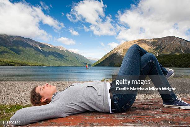 lake rotoiti is lake in the tasman region of new zealand. it is a mountain lake within in the nelson lakes national park. a girls lies down on a picnick lunch table and enjoys the sun - nelson lakes national park stock pictures, royalty-free photos & images