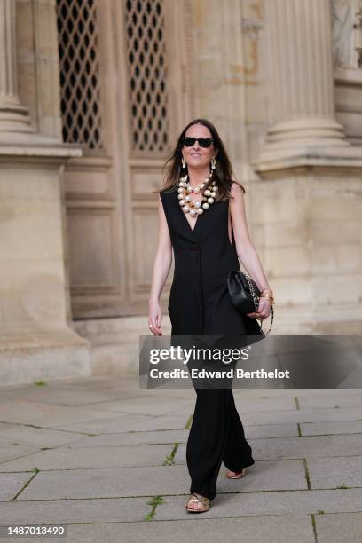 Alba Garavito Torre wears black sunglasses from Ray Ban, gold and white pendant earrings, a white latte and gold pearls large necklace, a black...