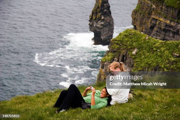 girls with camera on cliffs of moher with atlantic ocean below. - cliff stock-fotos und bilder