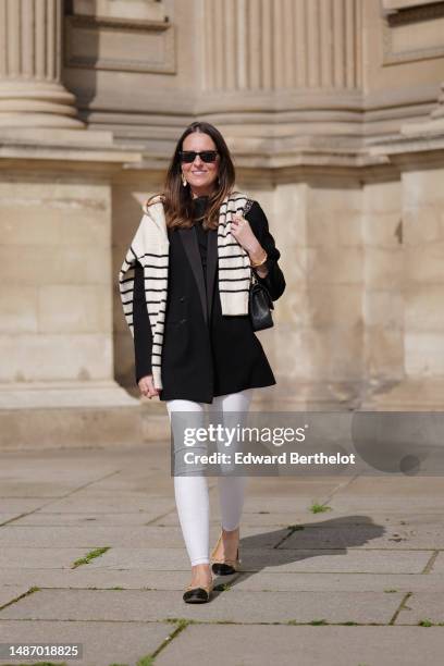 Alba Garavito Torre wears black sunglasses from Ray Ban, gold and white pendant large earrings, a black t-shirt, a white with black small striped...