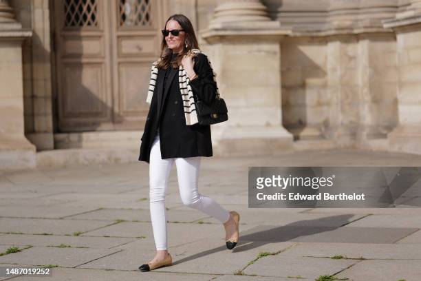 Alba Garavito Torre wears black sunglasses from Ray Ban, gold and white pendant large earrings, a black t-shirt, a white with black small striped...