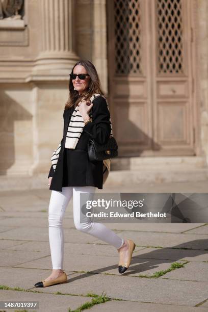 Alba Garavito Torre wears black sunglasses from Ray Ban, gold and white pendant large earrings, a black t-shirt, a white with black small striped...