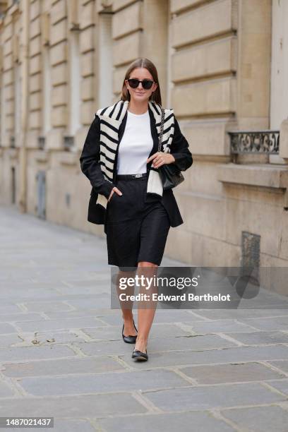 Diane Batoukina wears black large sunglasses, a white halter-neck tank-top from Anine Bing, a black blazer jacket from Massimo Dutti, a white latte...