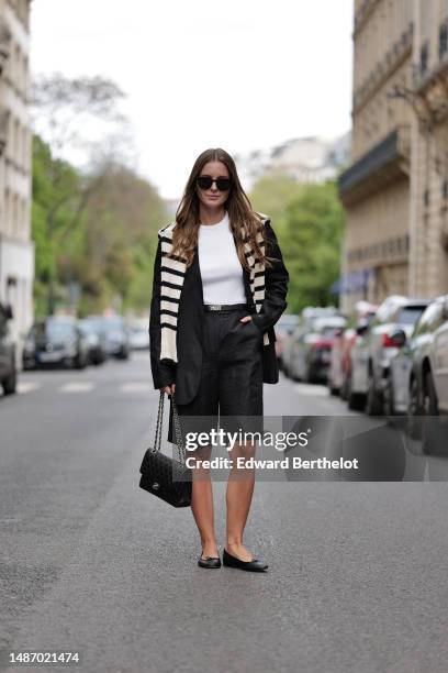 Diane Batoukina wears black large sunglasses, a white halter-neck tank-top from Anine Bing, a black blazer jacket from Massimo Dutti, a white latte...