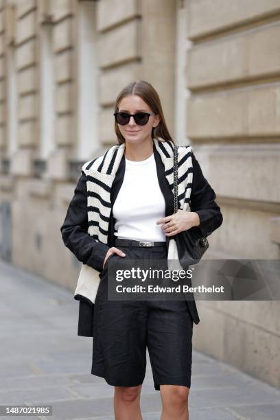 Diane Batoukina wears black large sunglasses, a white halter-neck tank-top from Anine Bing, a black blazer jacket from Massimo Dutti, a white latte...