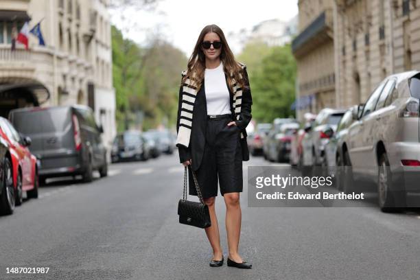 Diane Batoukina wears black large sunglasses, a white halter-neck tank-top from Anine Bing, a black blazer jacket from Massimo Dutti, a white latte...