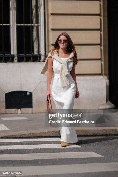 Diane Batoukina wears dark brown large squared sunglasses from Dior, a white square-neck / linen belted long dress, a white latte ribbed wool...