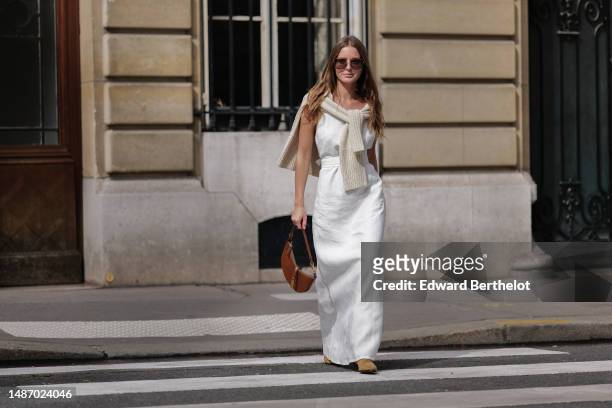 Diane Batoukina wears dark brown large squared sunglasses from Dior, a white square-neck / linen belted long dress, a white latte ribbed wool...