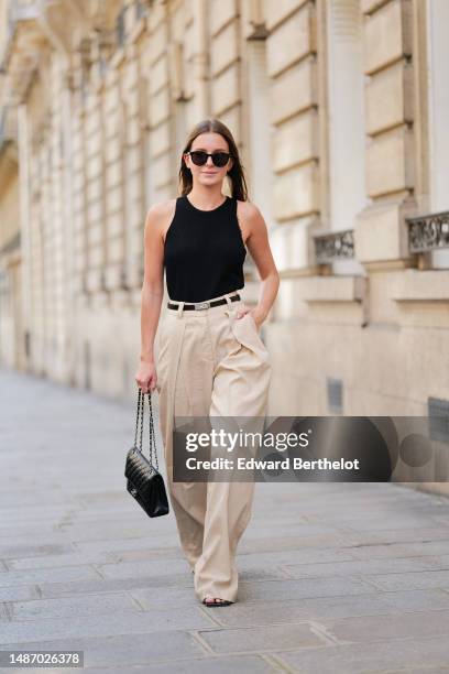 Diane Batoukina wears black circle sunglasses, a black ribbed halter-neck tank-top, a black shiny leather and silver buckle Kelly belt from Hermes,...