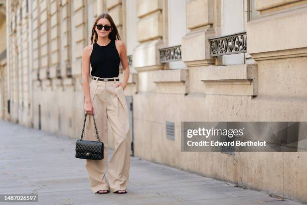 Diane Batoukina wears black circle sunglasses, a black ribbed halter-neck tank-top, a black shiny leather and silver buckle Kelly belt from Hermes,...