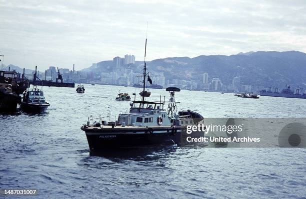 Junks and boats between Kowloon and Hong Kong overlooking the city here a police boat, July 1968.