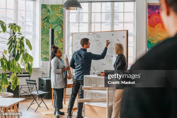 businessman explaining female colleagues while drawing and discussing over white board at office - tormenta de ideas fotografías e imágenes de stock