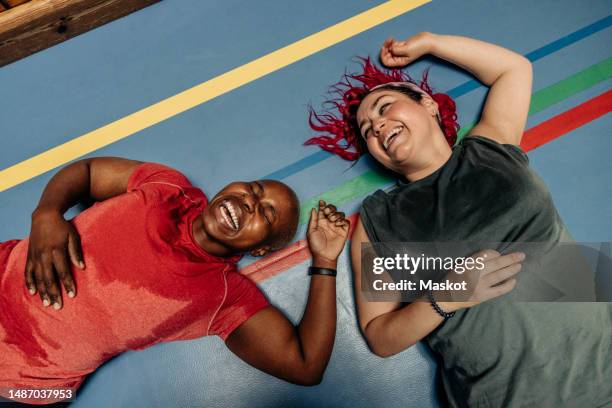 high angle view of female athletes laughing while lying on safety mat at sports court - schweiß stock-fotos und bilder