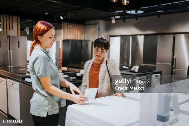 saleswoman advising female customer in buying washing machine at electronics store - buying washing machine stockfoto's en -beelden