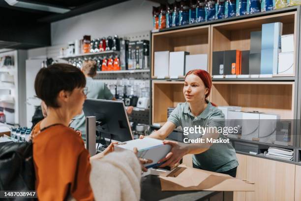 female customer giving appliance box to sales clerk at checkout counter in electronics store - electronic products stock pictures, royalty-free photos & images