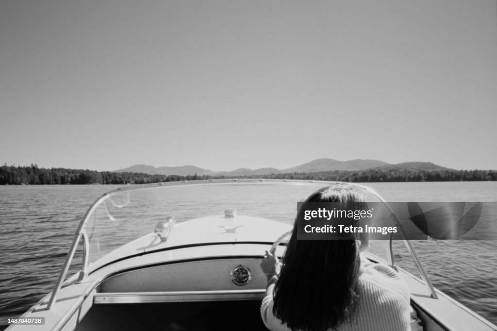 United States, New York, Santa Clara, Rear view of woman driving motorboat on Upper Saranac Lake, black and white