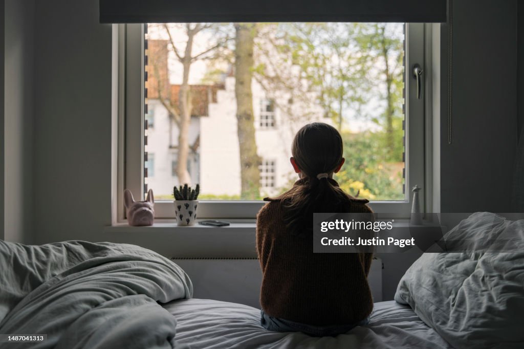 Powerful portrait of a young girl looking out of her bedroom window