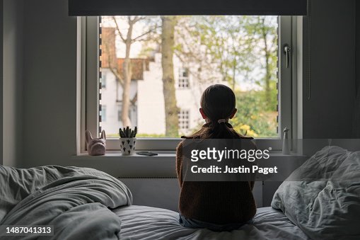 Powerful portrait of a young girl looking out of her bedroom window