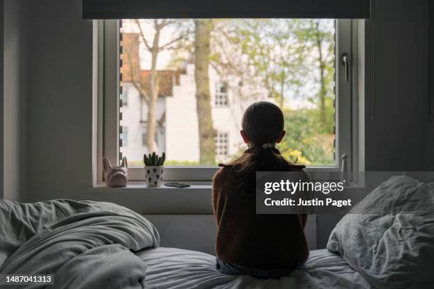 powerful portrait of a young girl looking out of her bedroom window - person on phone stock pictures, royalty-free photos & images