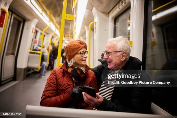 smiling senior couple using a mobile phone on a subway train - tunnelbana bildbanksfoton och bilder