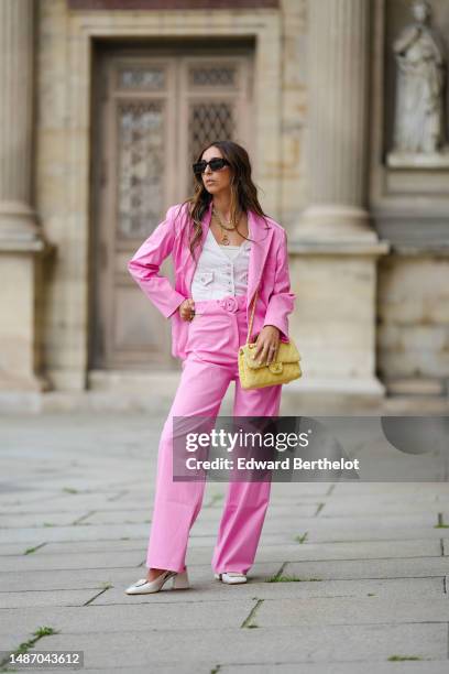 Gabriella Berdugo wears black marble print pattern squared sunglasses, gold earrings, gold and silver pendant chain necklaces, a gold large necklace,...