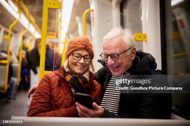 lachendes älteres paar mit einem mobiltelefon in einer u-bahn - nahverkehr stock-fotos und bilder