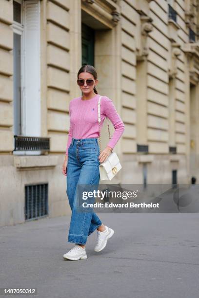 Diane Batoukina wears dark brown large squared sunglasses from Dior, a pale pink braided wool pullover from Ralph Lauren, blue faded denim / buttons...