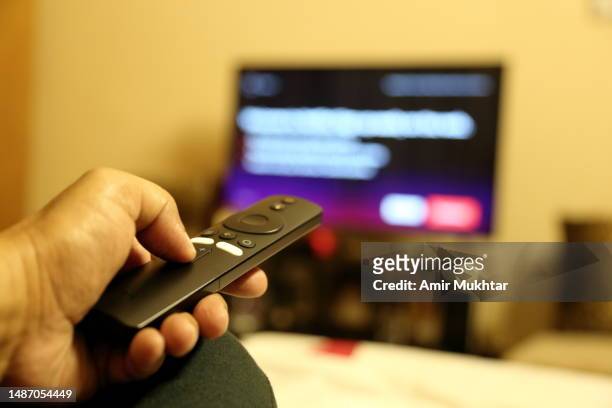 closeup of a human hand pointing remote control towards high-definition television (hd tv). - smart tv - fotografias e filmes do acervo